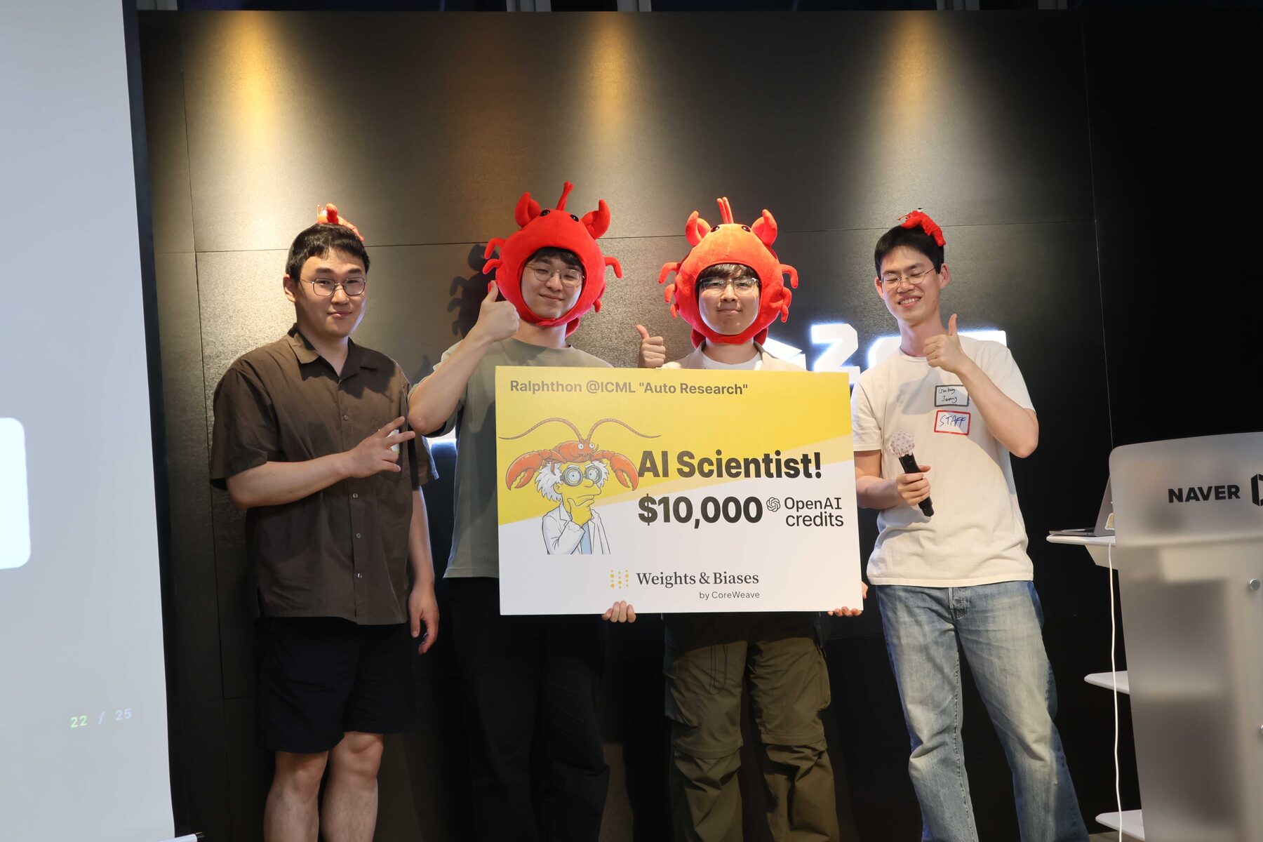 Team WooandB on stage at Ralphthon@ICML wearing red lobster hats, holding the AI Scientist first-place board for $10,000 in OpenAI credits.